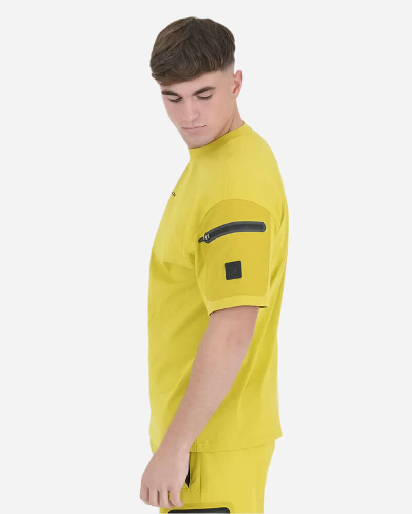 Model wearing Acid Mustard Peaceful Hooligan FORGE T Shirt with sleeve pocket, showcasing urban fashion style.