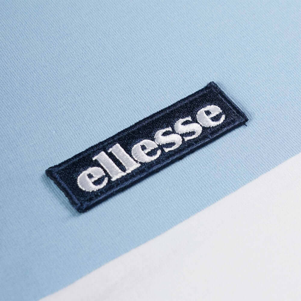 Close-up of Ellesse logo on a light blue t-shirt from the Live Forever Collection, showcasing brand detail.