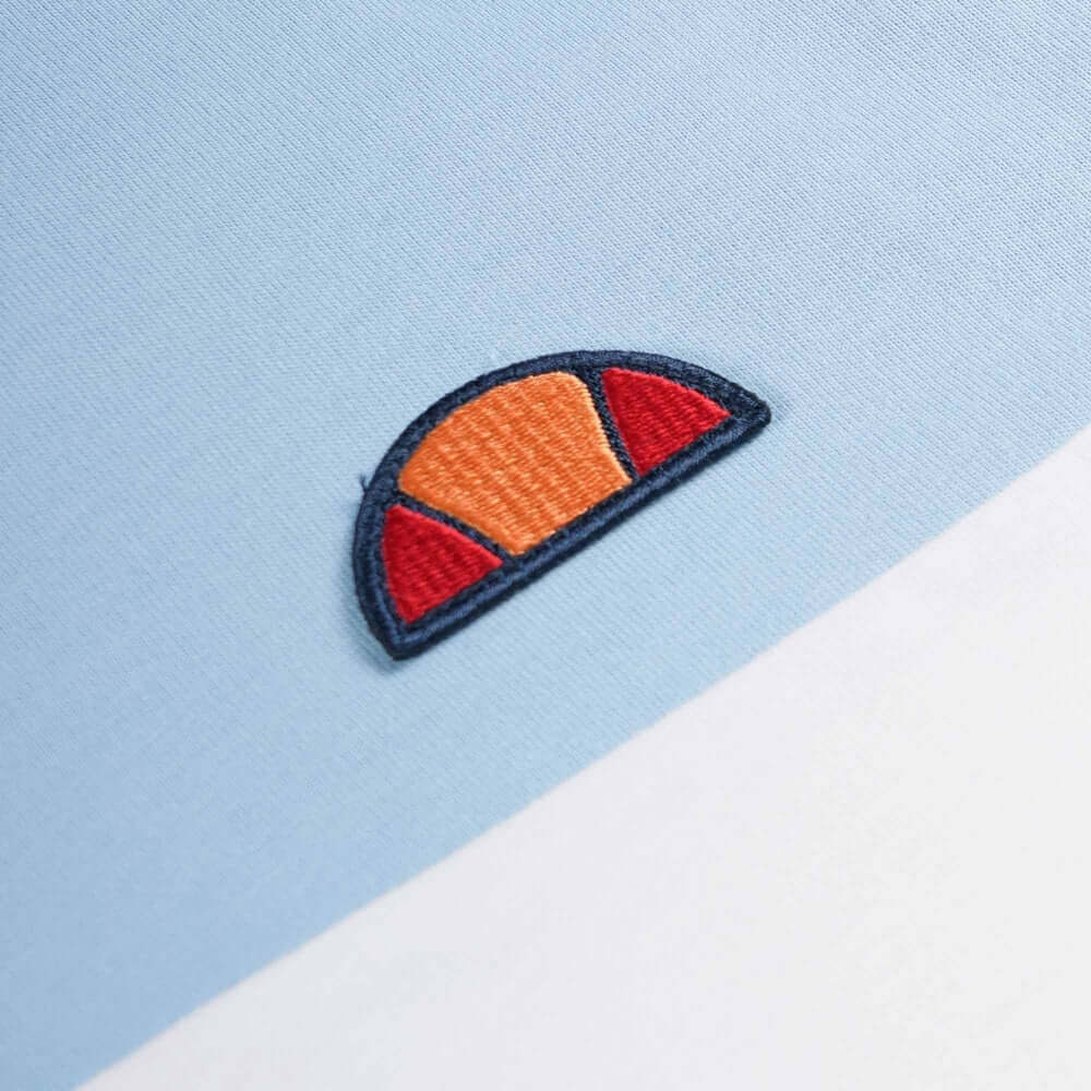 Close-up of embroidered Ellesse logo on a light blue T-shirt from the Live Forever Collection.