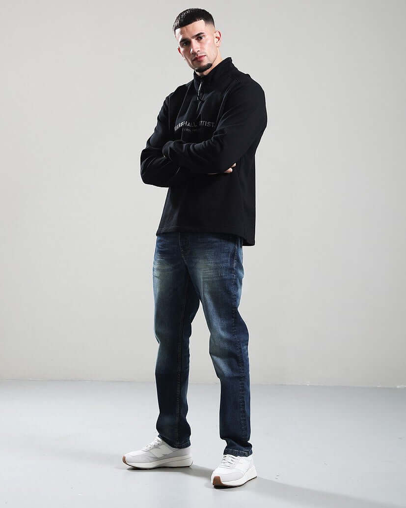 Model wearing Marshall Artist MICROSPHERE 1/4 Zip Sweat in black with jeans and sneakers, showcasing street style.