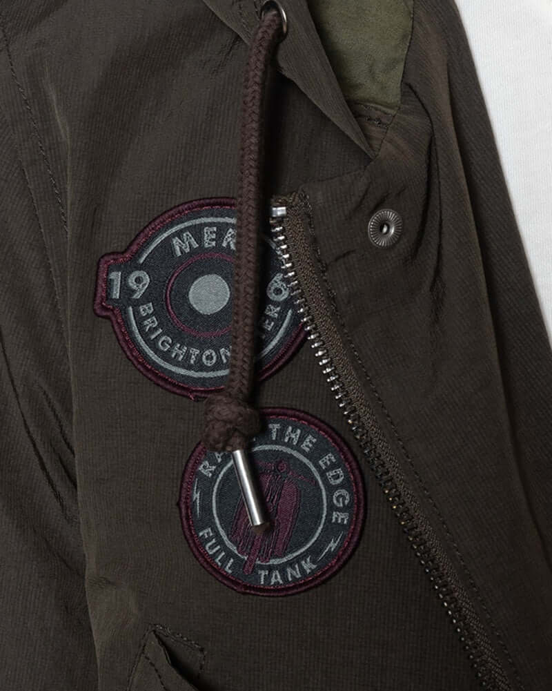 Close-up of Merc DEFOE Parka Jacket Dark Khaki featuring badges and zipper details.