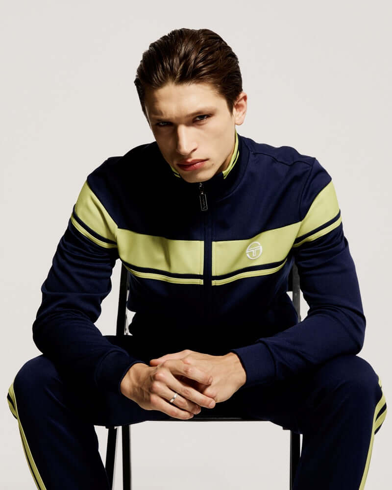 Sergio Tacchini DAMARINDO Track Top Maritime Blue/ Celery Green worn by a model sitting on a chair.